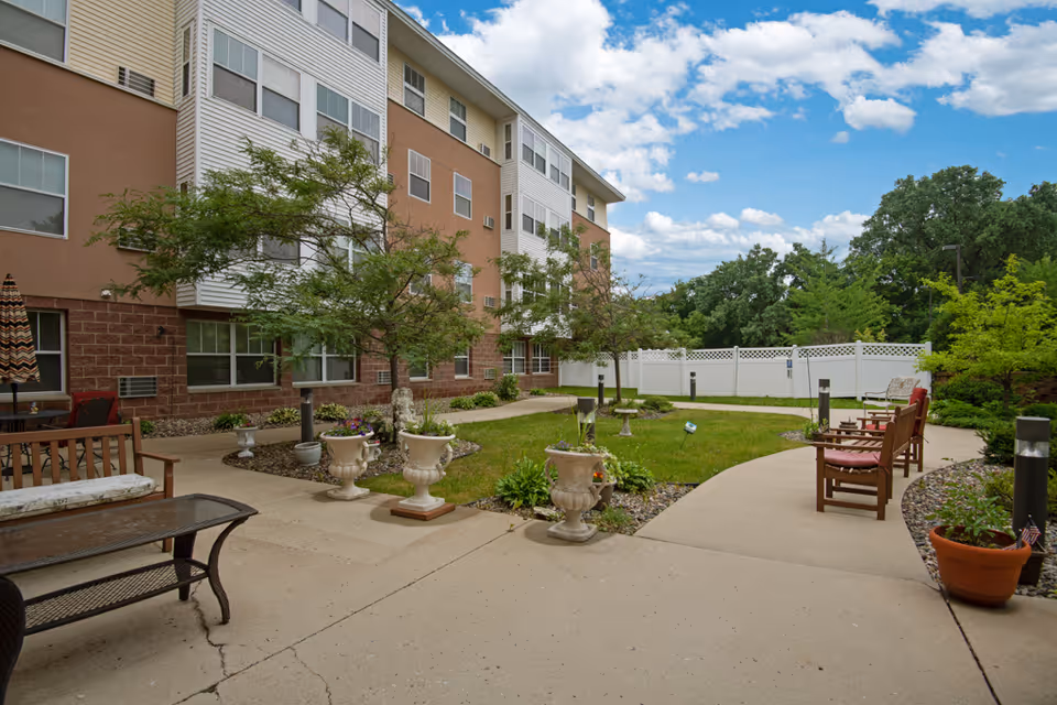 Outdoor courtyard of a multi-story senior living building with benches, planters, a lawn and a paved walkway.