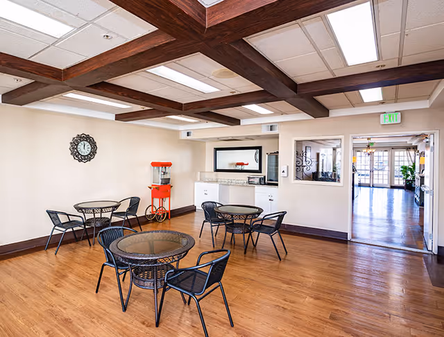 Communal dining area with round glass-top tables and chairs, a popcorn machine, and a wood-beamed ceiling.