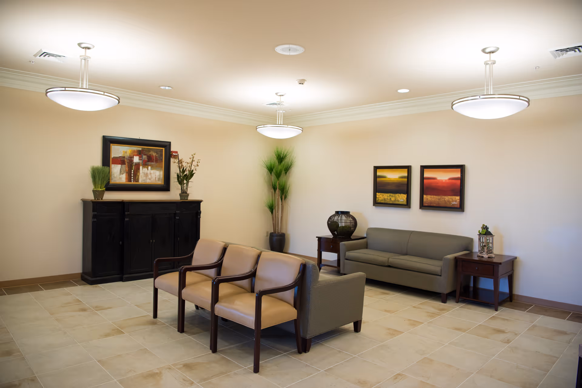 A well-lit waiting room with chairs, a sofa, side tables, wall art, and decorative plants.