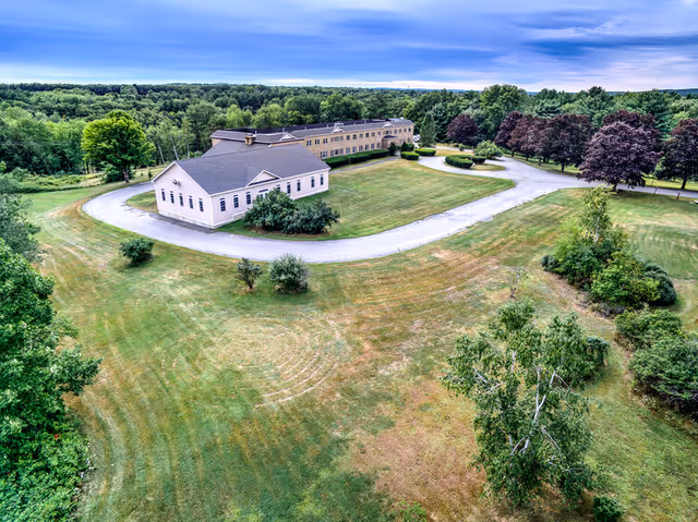 Aerial view of a retirement community's buildings with a curved driveway, expansive lawns, and surrounding trees.