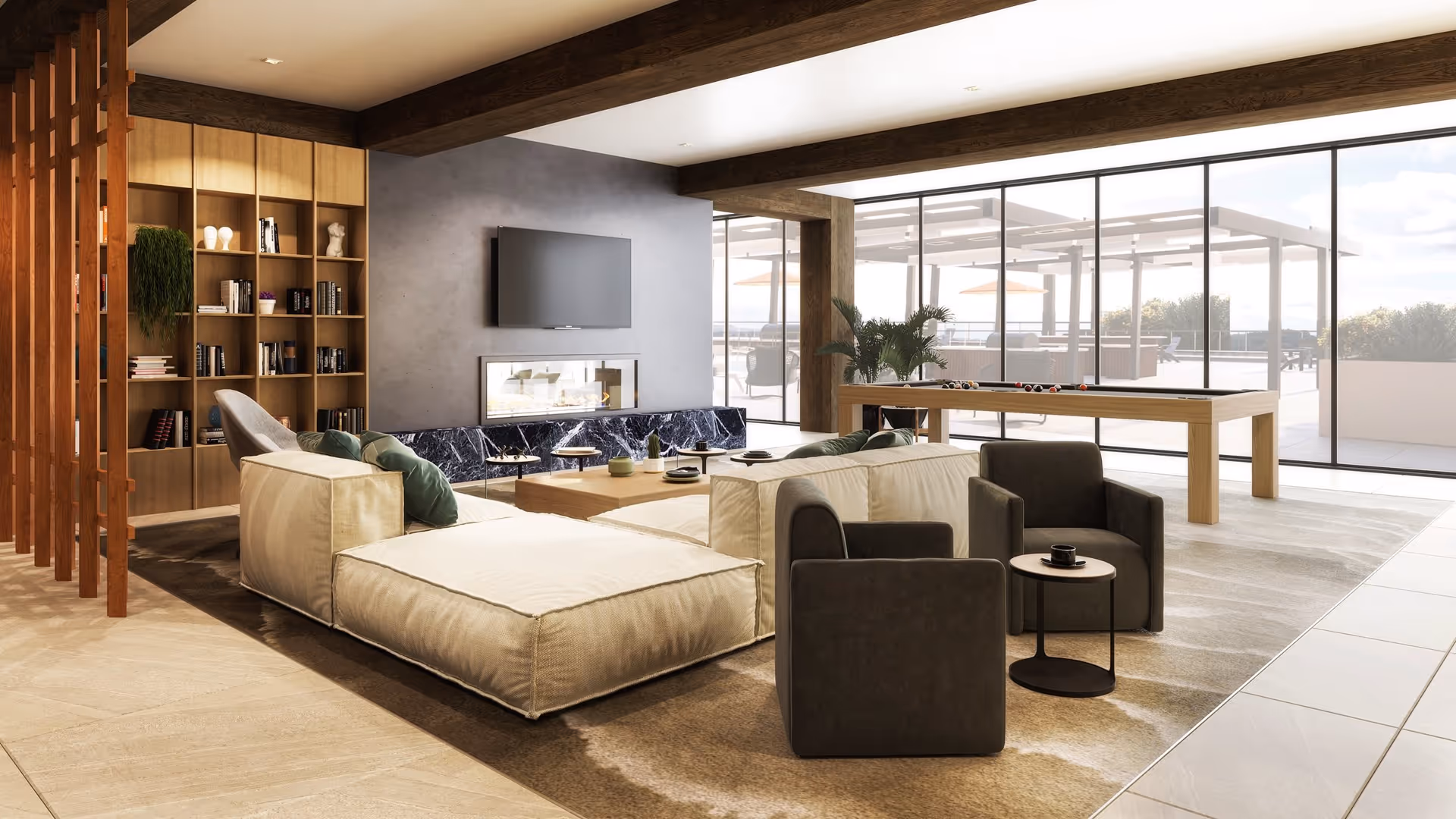 Spacious modern common lounge with low sectional sofas and armchairs, a TV above a fireplace, bookshelf, and a pool table beside floor-to-ceiling windows overlooking a terrace.