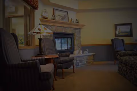 Cozy living room with stone fireplace, armchairs, and framed art in a senior facility.