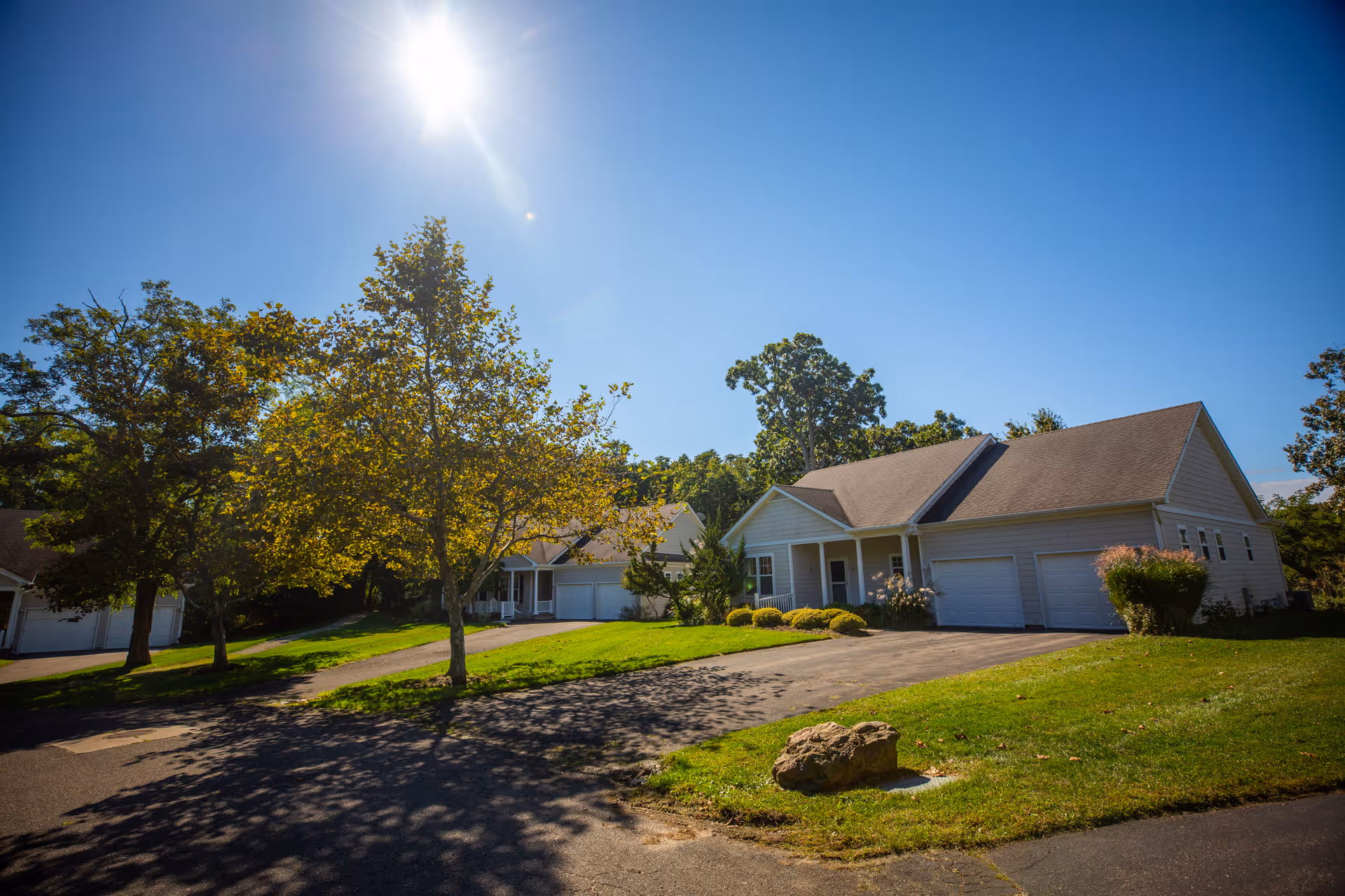 Sunny day view of a residential area at Peconic Landing with single-story houses, green lawns, trees, and a clear blue sky.