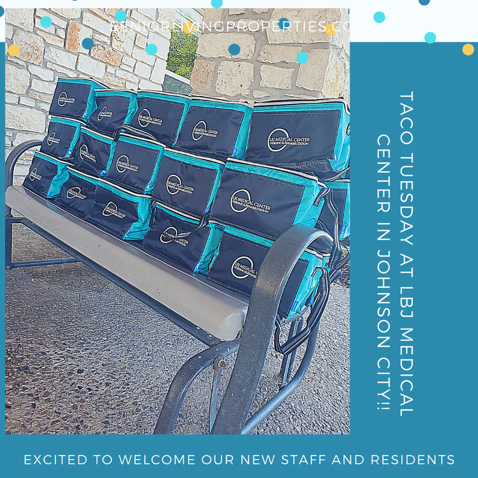 A metal bench with a beige seat cushion is stacked with multiple insulated lunch bags branded with LBJ Medical Center Nursing & Rehabilitation logo, placed outdoors against a stone wall.