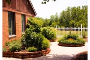 Brick building exterior with manicured shrubs, circular brick planters, and a white fence in the courtyard.