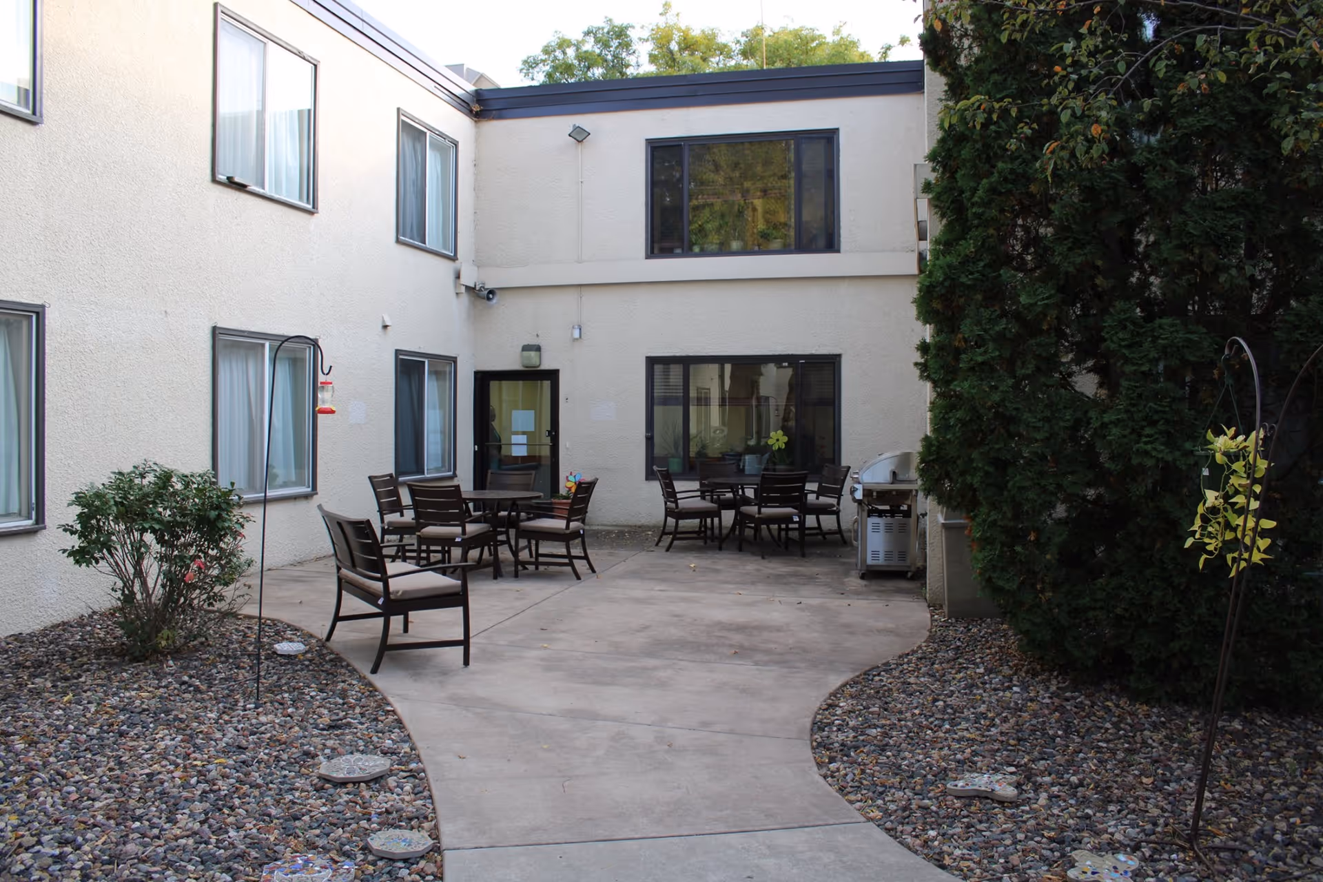 Enclosed courtyard with patio tables and chairs, a grill, and surrounding two-story building windows and doors.
