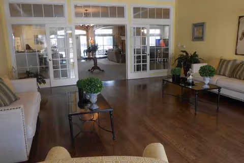 Bright living room in a senior care facility with couches, glass doors, and plants.