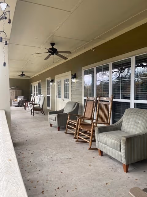 Covered porch with rocking chairs, upholstered armchairs, ceiling fans, and windows along the building.