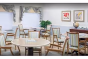 Bright communal dining area with round tables, wooden chairs, framed artwork, and windows with valances.