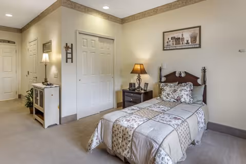 Bright, neatly furnished bedroom with a single bed, nightstand and lamp, closet doors and a small hallway.