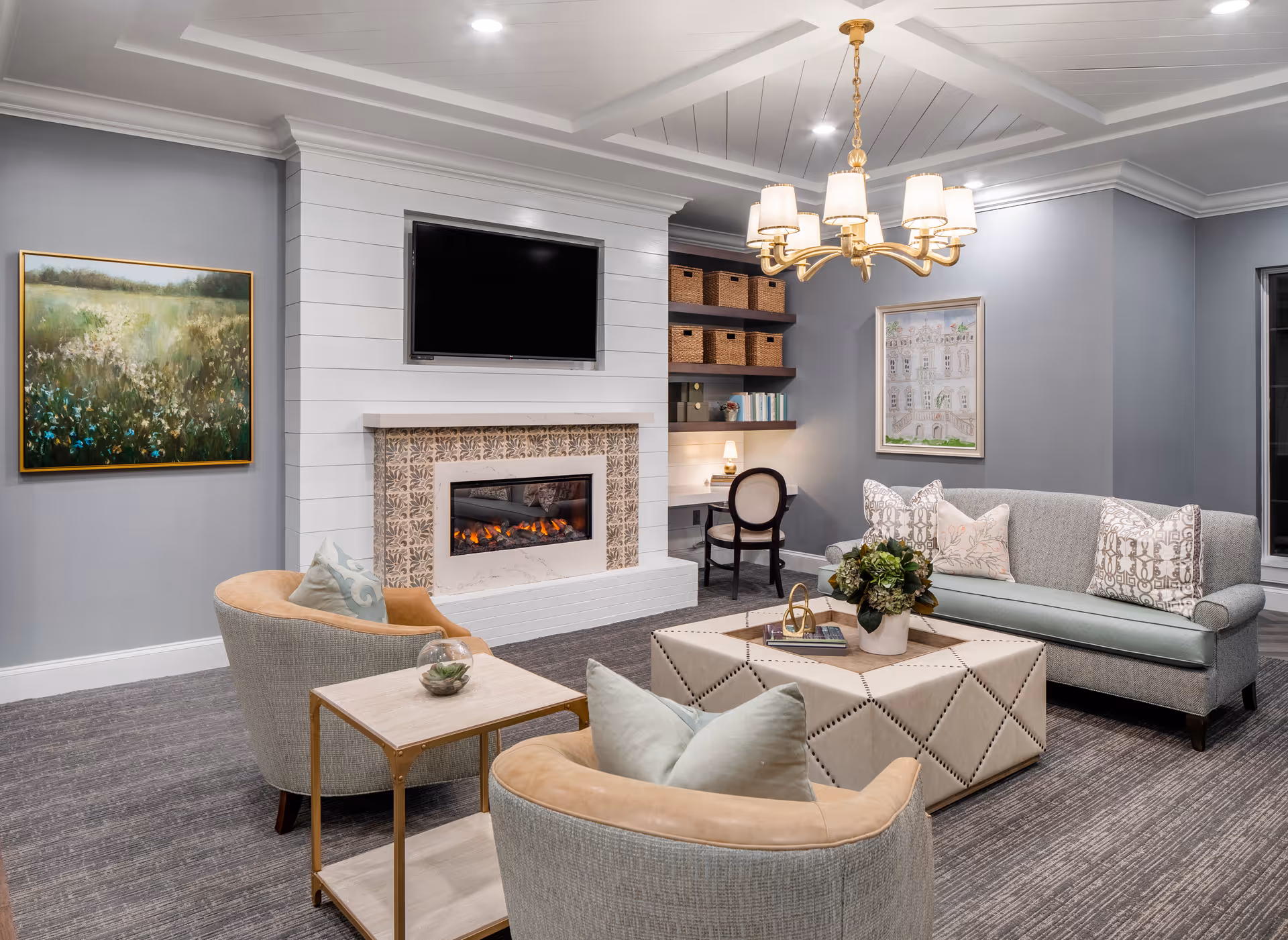 Well-appointed common living room with a fireplace, wall-mounted TV, chandelier, and a seating area with sofas and chairs.