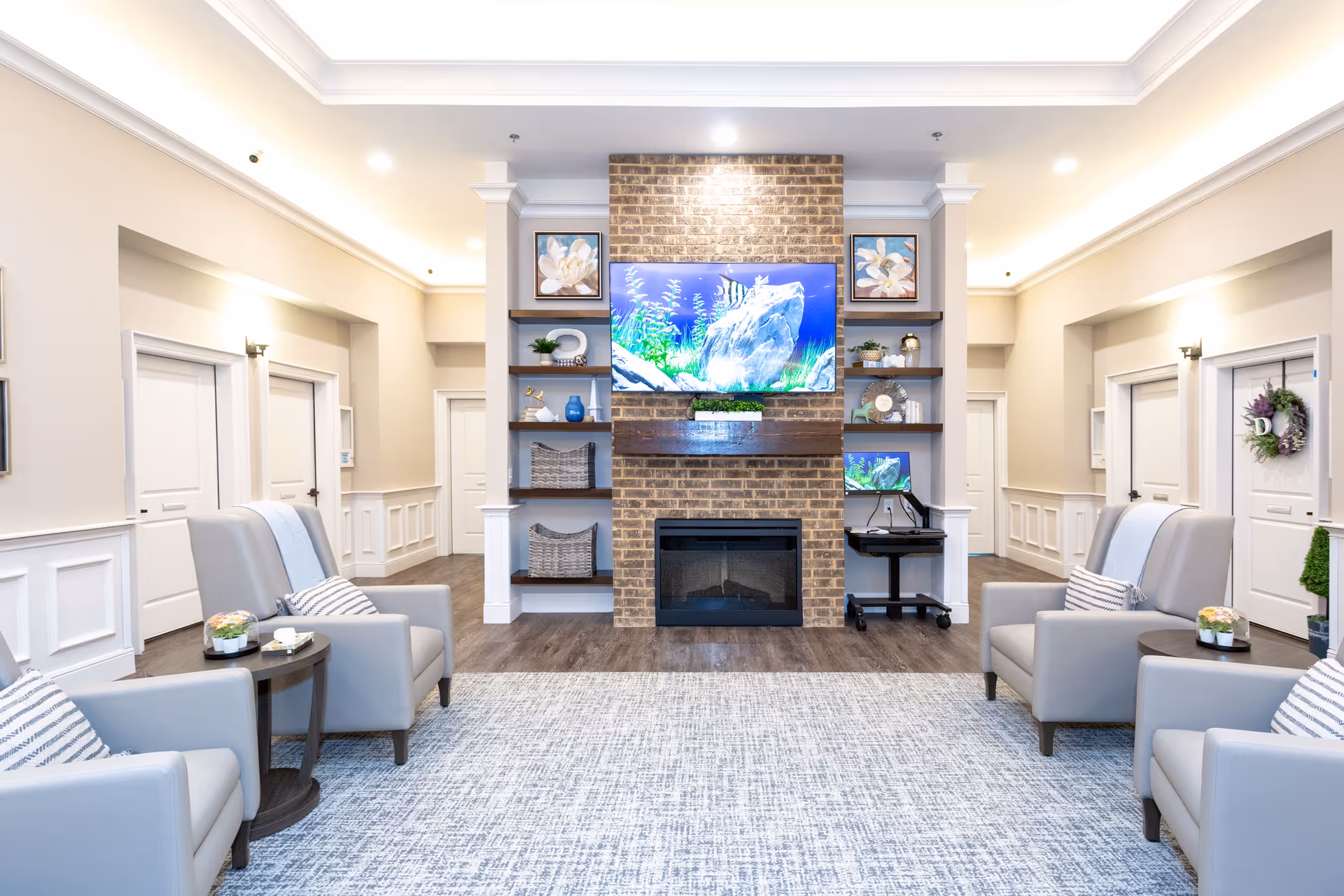 Bright modern sitting room with a central brick fireplace and wall-mounted TV flanked by shelves and armchairs.