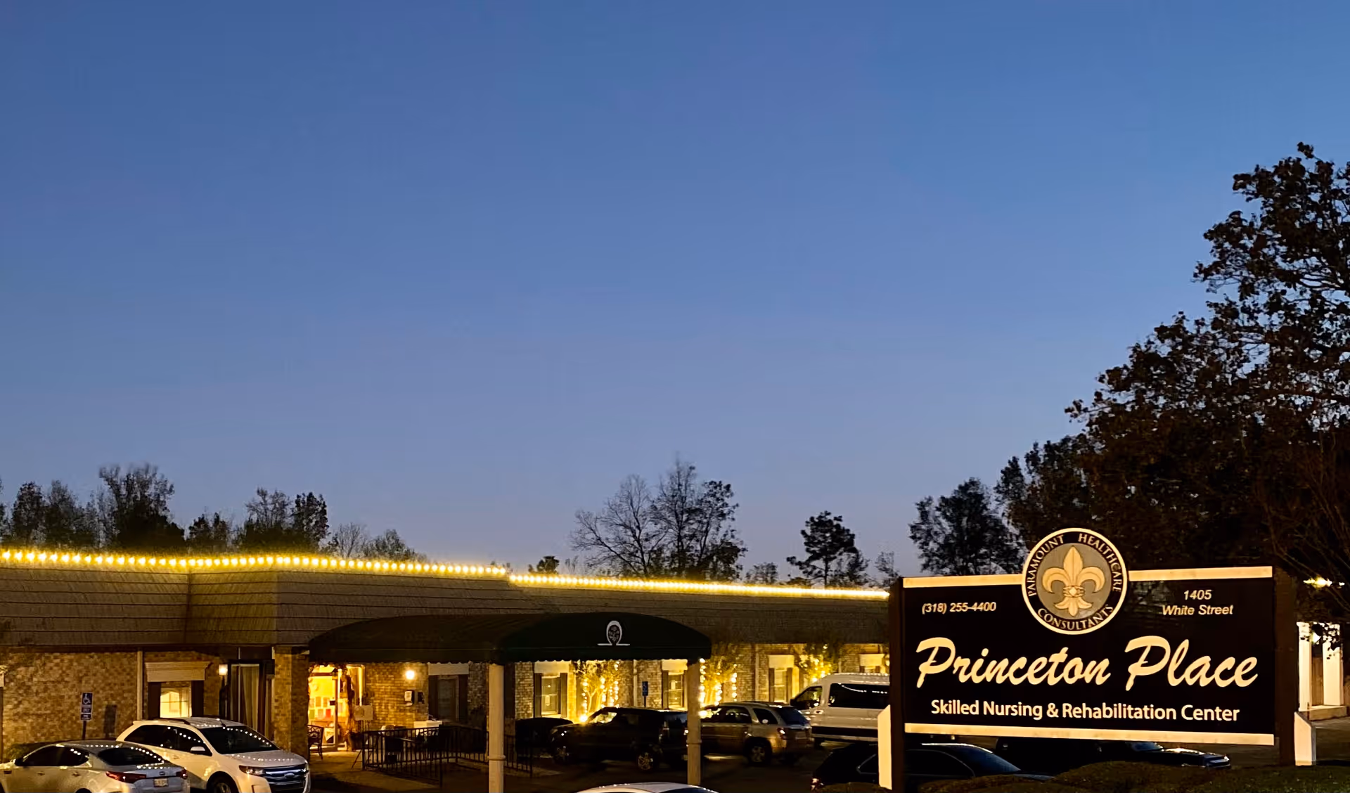 Exterior front view of Princeton Place Skilled Nursing & Rehabilitation Center at dusk with illuminated sign and entrance.