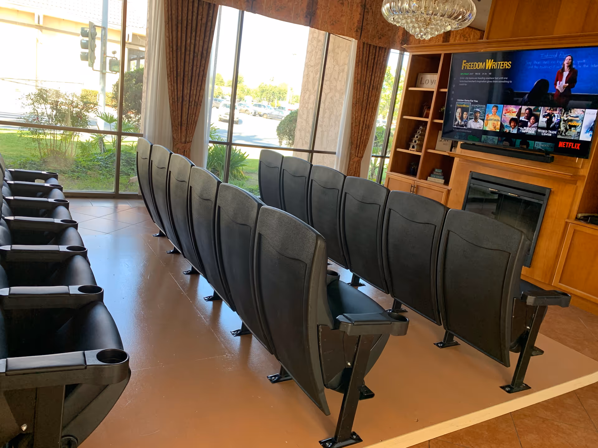 Rows of black theater-style chairs face a large TV in a sunny lounge.