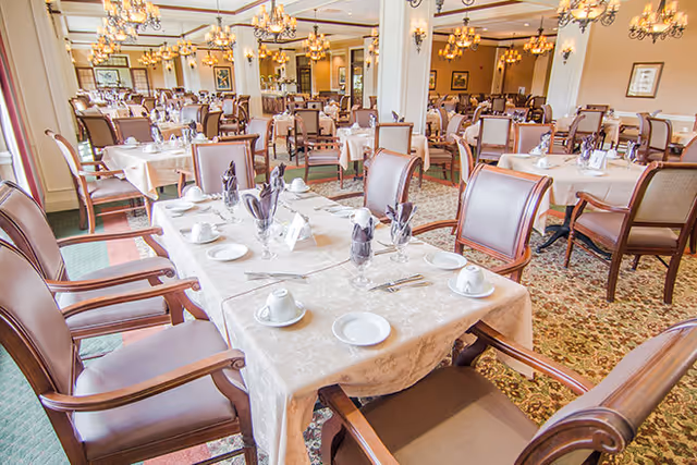 Formal dining room with multiple set tables, upholstered chairs, and chandeliers.
