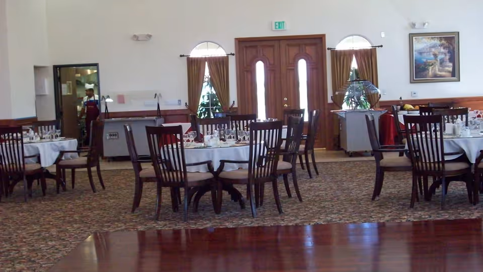 Spacious dining room with round tables set for a meal and wooden chairs on patterned carpet.