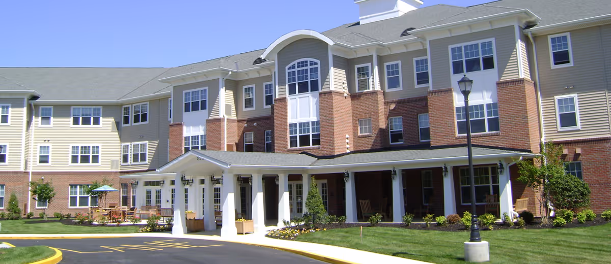Front exterior of a three-story senior living building with a covered entrance, white columns, and landscaped lawn.