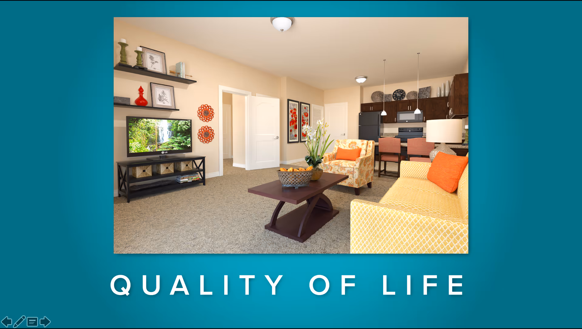 A cozy living room and kitchen area in a senior living facility featuring a yellow patterned sofa with orange cushions, a floral armchair, a wooden coffee table with a basket and flowers, a TV on a stand with shelves, and a kitchen with dark cabinets, a refrigerator, stove, and two pendant lights over a breakfast bar with two chairs.