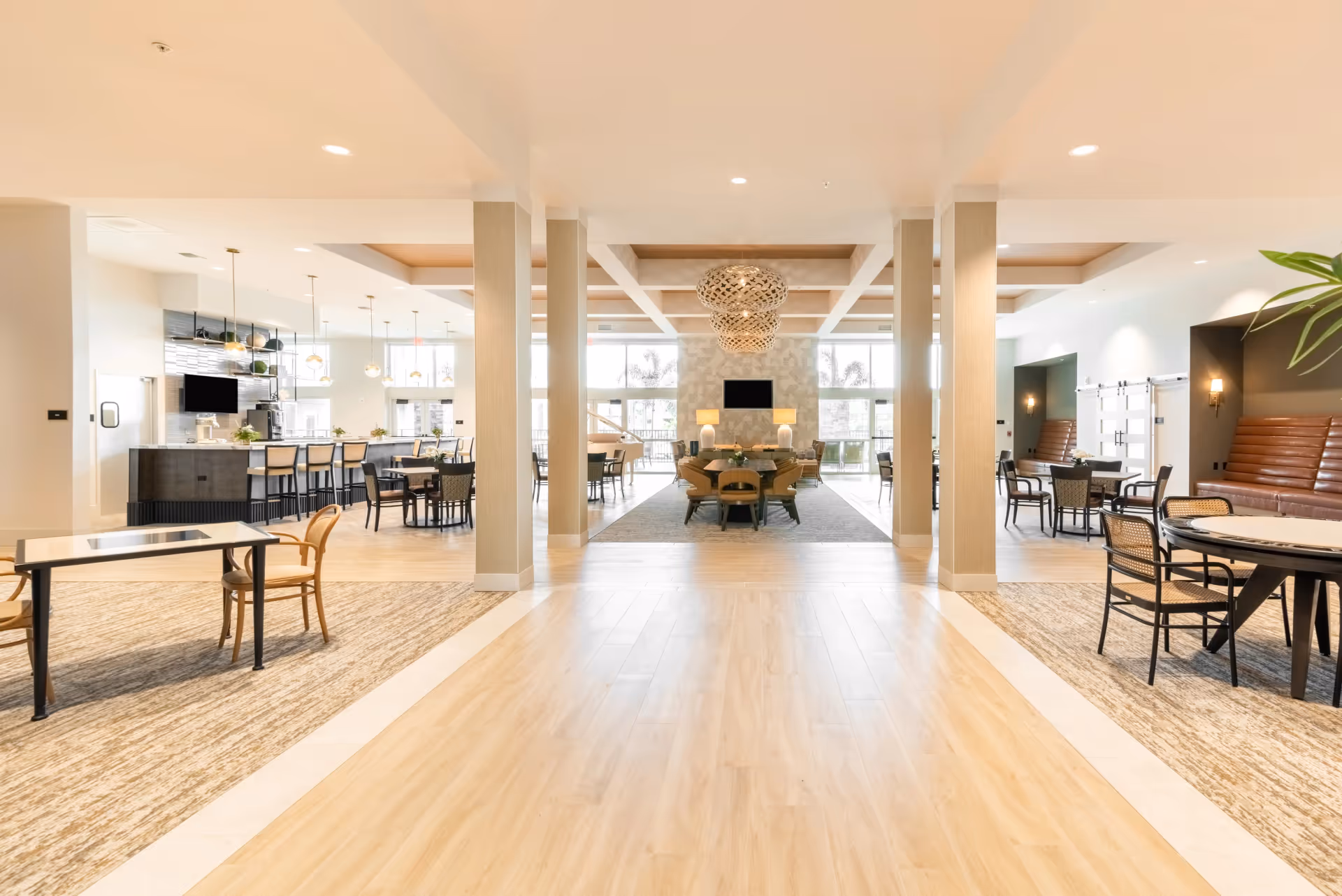 Spacious bright communal dining and lounge area with tables, chairs, a kitchen bar, and decorative lighting.