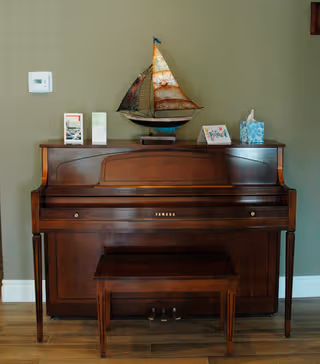 A wooden Yamaha upright piano with a matching bench and decorative items on top against a neutral wall.