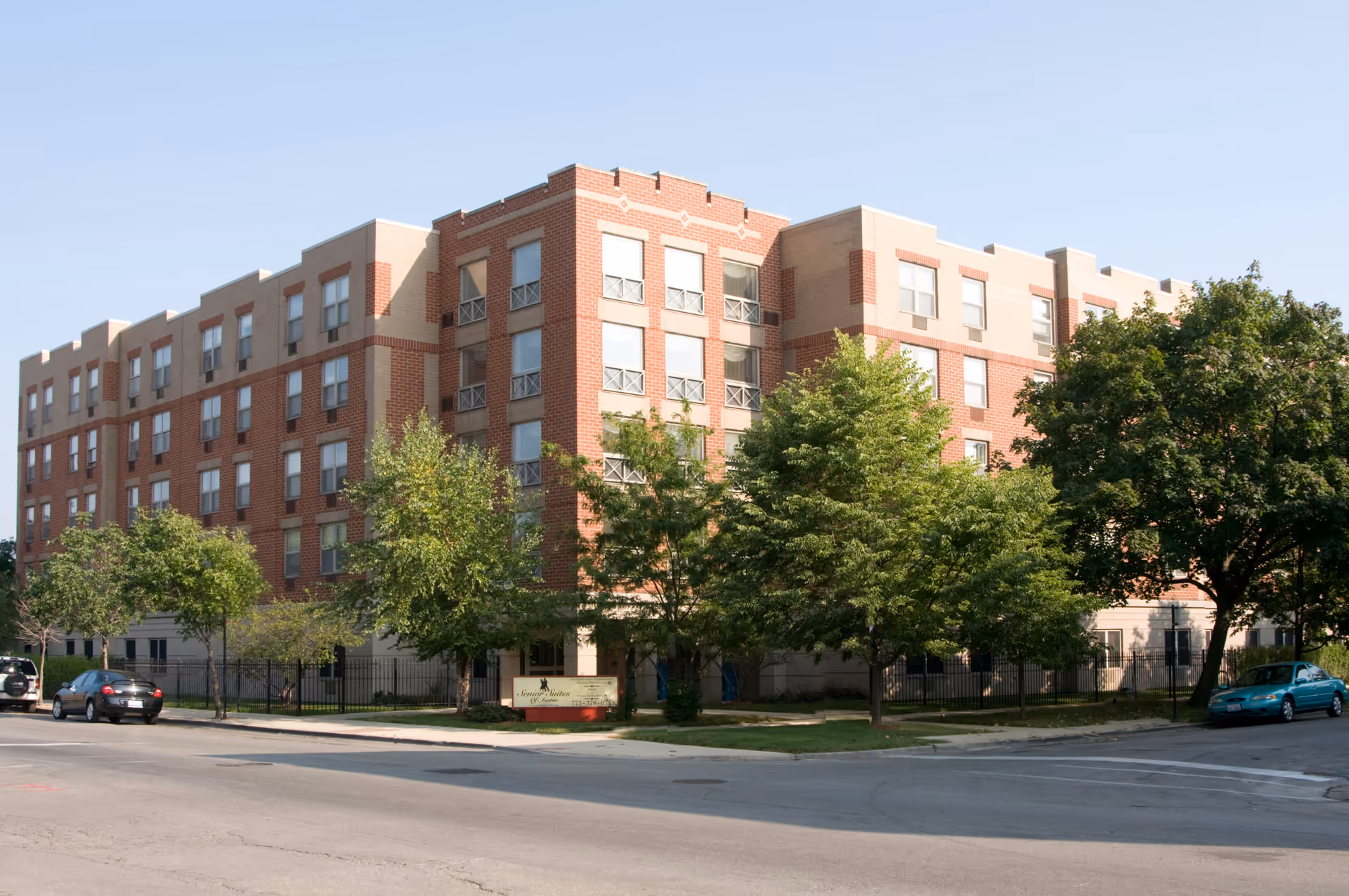 Multi-story brick senior living building with trees and parked cars along the street.