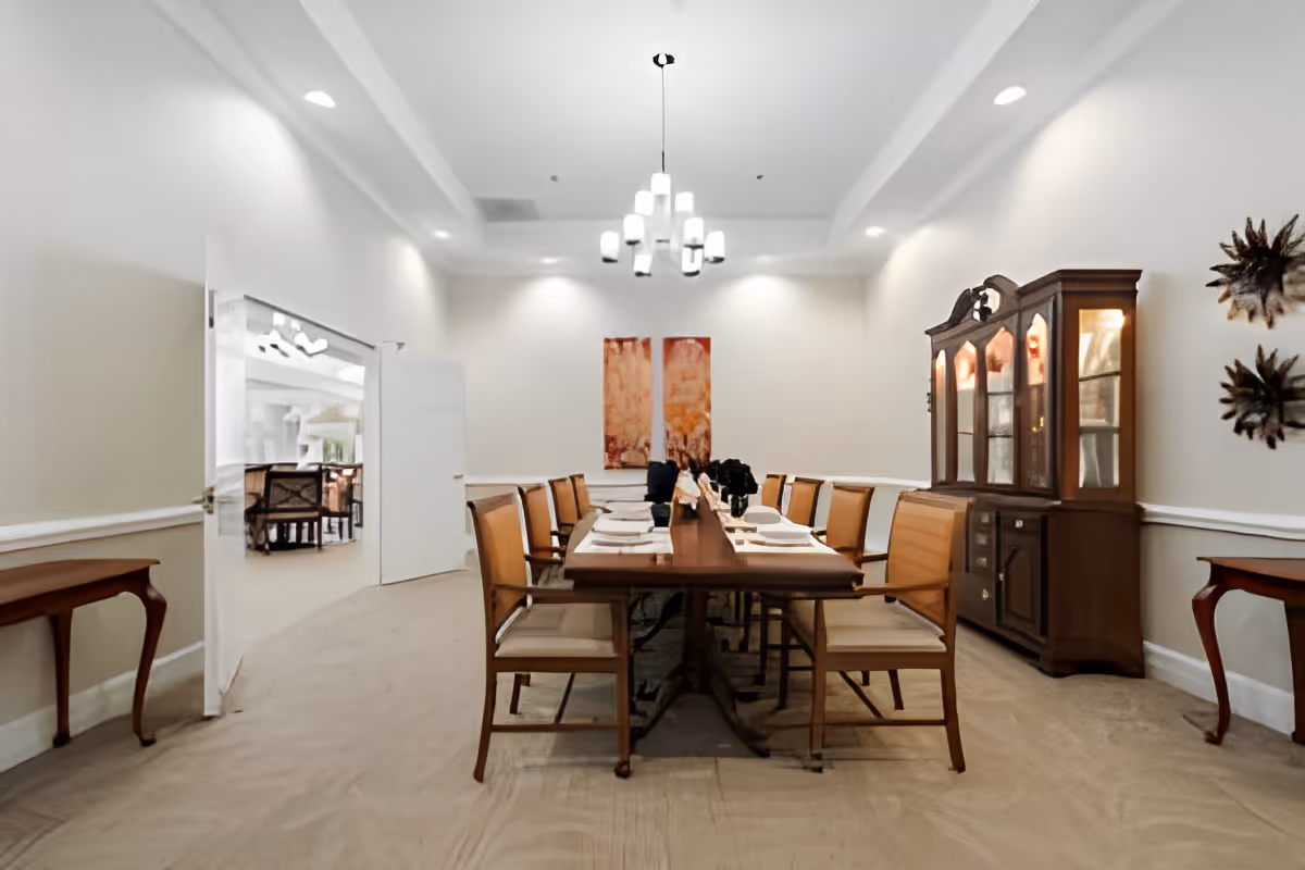 A formal dining room with a long wooden table set for a meal, surrounded by chairs and a china cabinet against the wall.