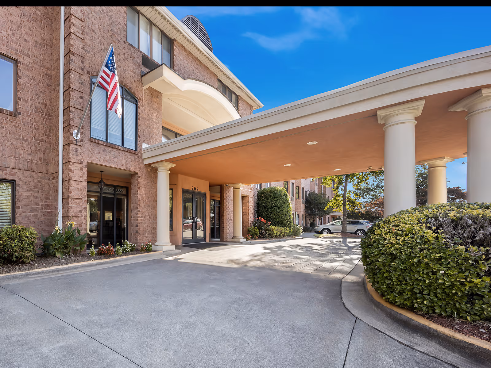 Brick senior living facility exterior with covered entrance and American flag.
