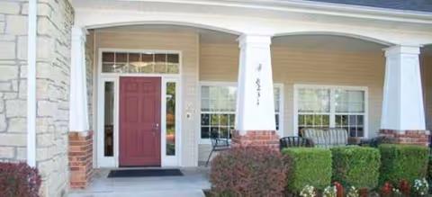 Front entrance of a senior living facility with a red door, columns, and seating.
