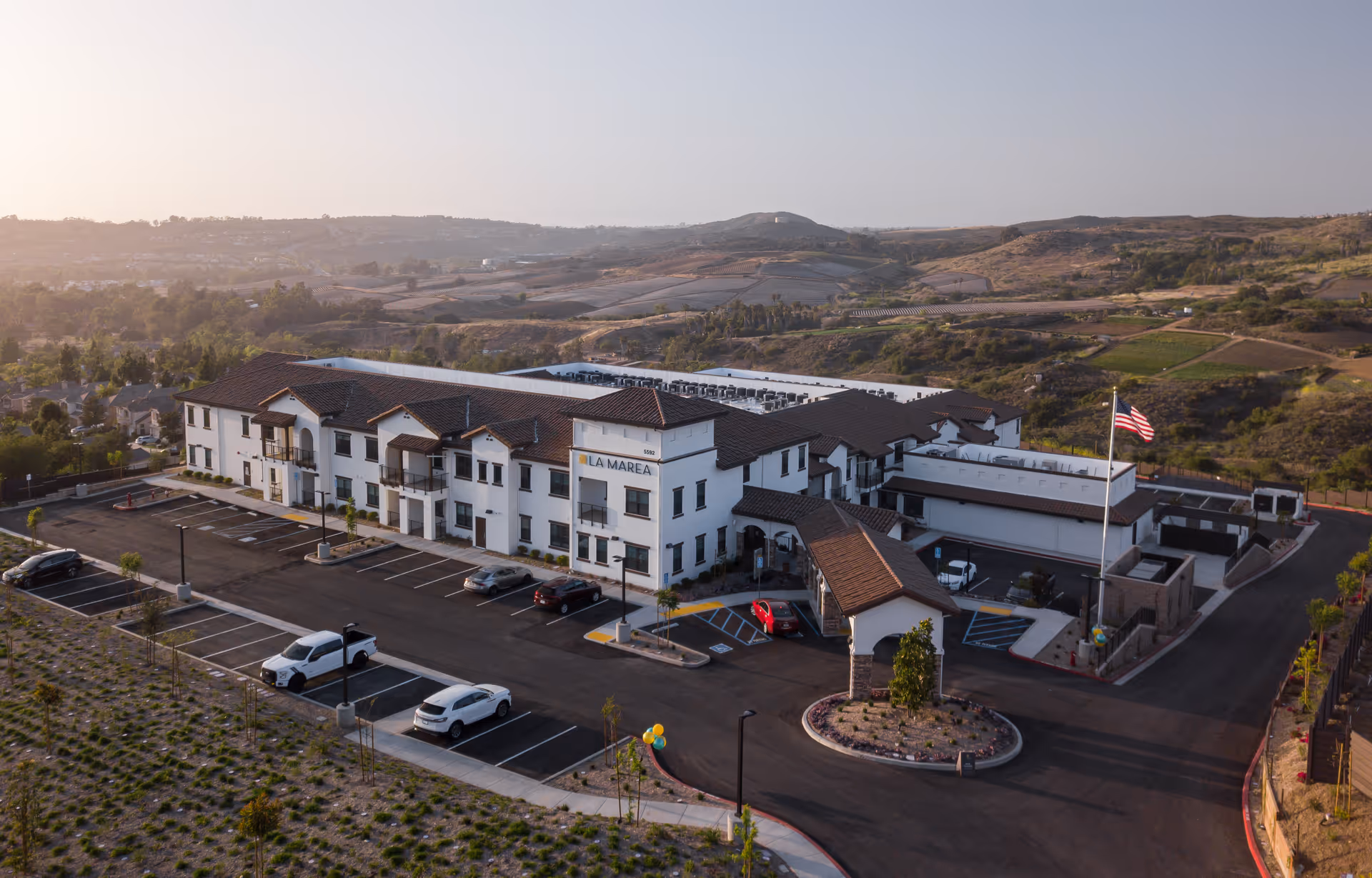 Aerial view of the La Marea Senior Living building with its parking lot and surrounding rolling hills.