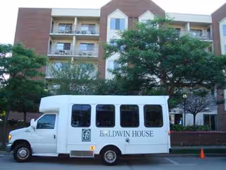 A white Baldwin House shuttle bus parked in front of a brick senior living building