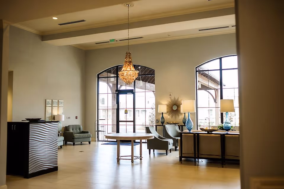 Spacious reception lobby with a chandelier, arched glass doors and windows, seating areas, and decorative lamps.