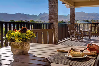 Outdoor patio dining area with table, chairs, potted plant, and mountain view.