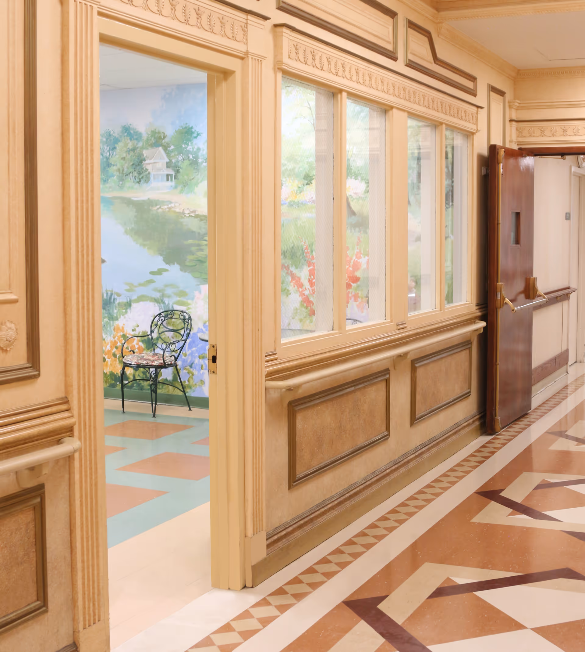 Decorative interior hallway with patterned floor and paneled walls, an open door revealing a mural and a wrought-iron chair.