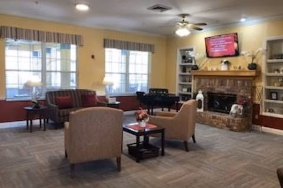 Cozy common living room with armchairs, a sofa, a brick fireplace, and a wall-mounted TV.