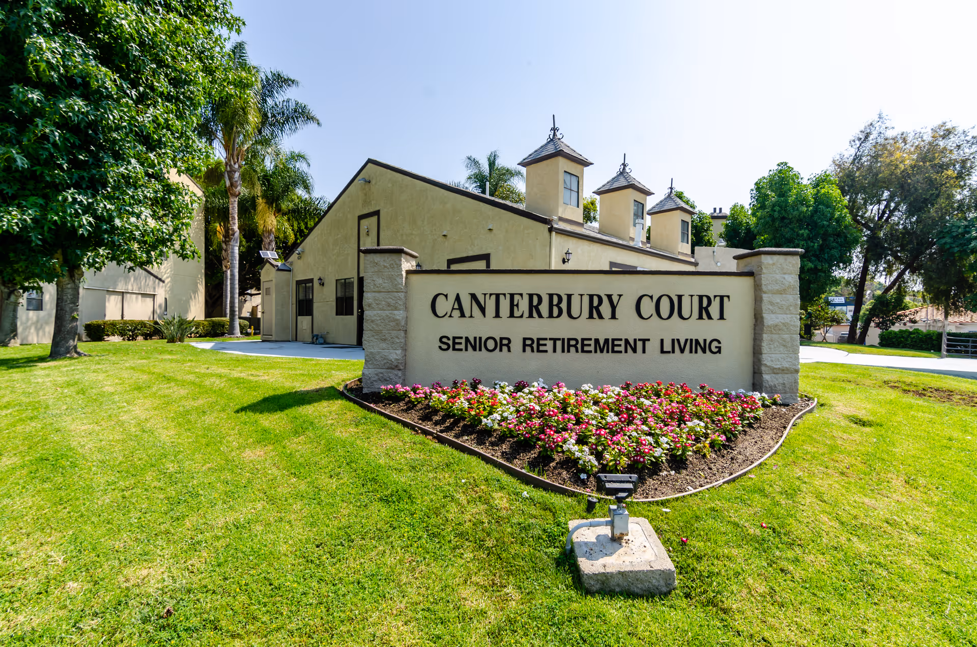 Stone entrance sign reading "Canterbury Court Senior Retirement Living" in front of a landscaped lawn and apartment building.