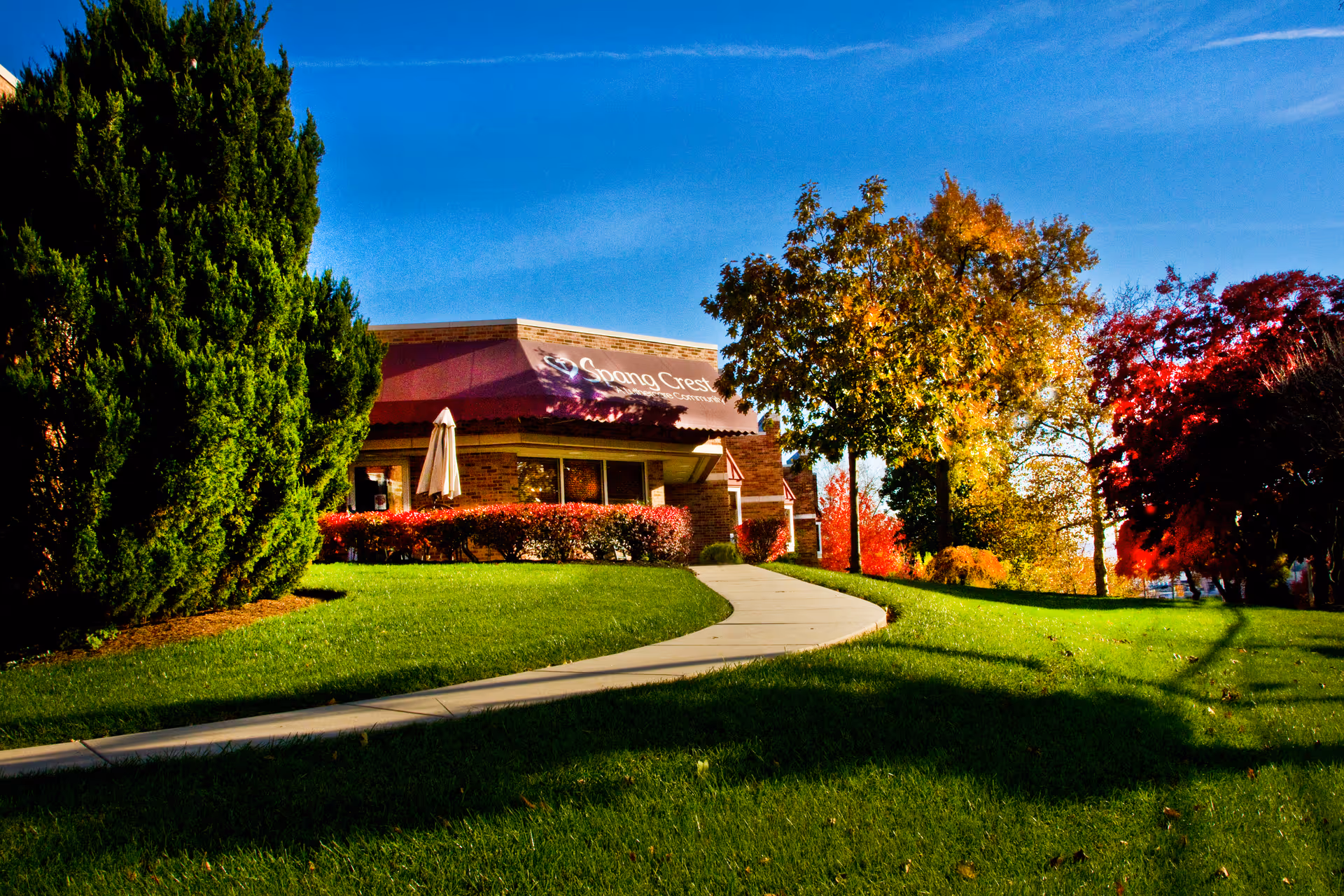 Exterior view of a healthcare building with a curved sidewalk, green lawn, and colorful autumn trees.