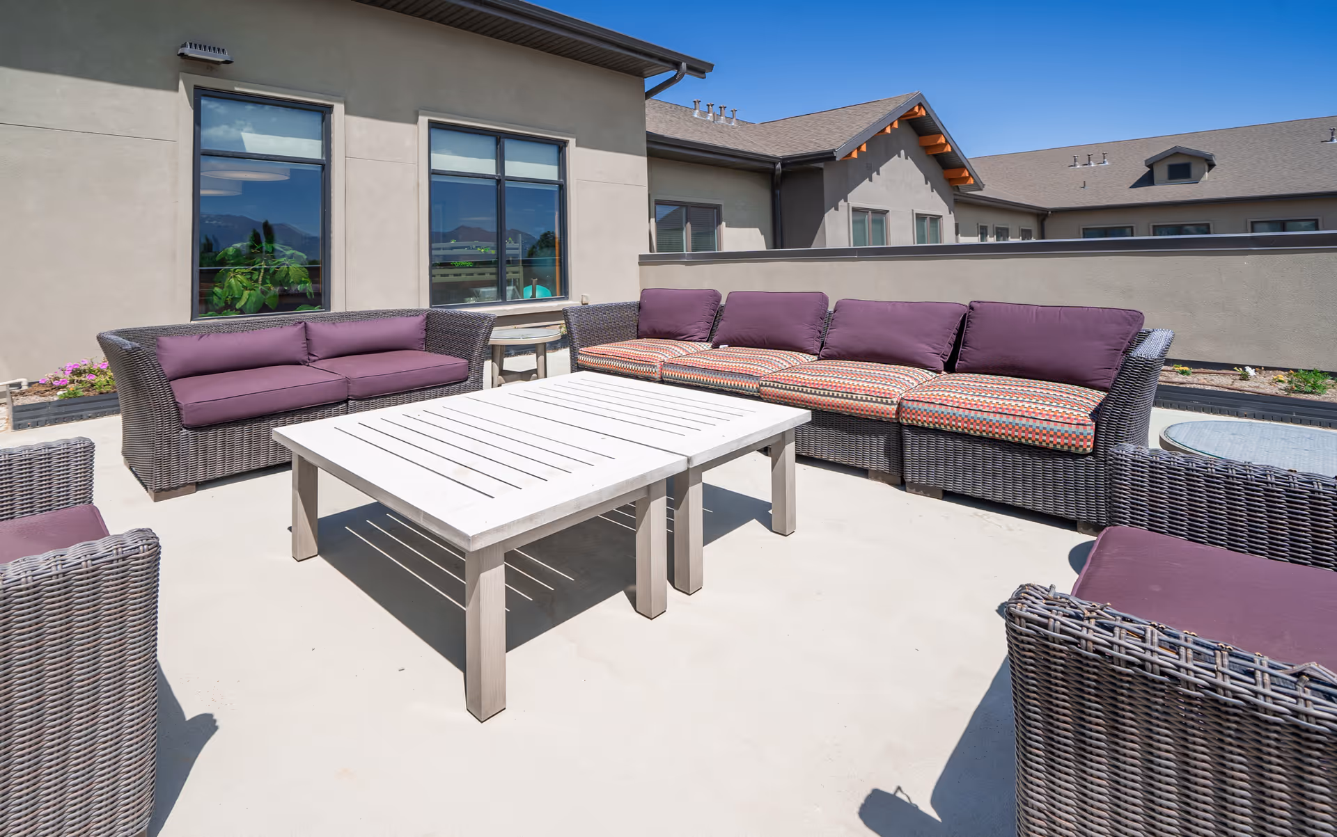 Outdoor rooftop patio with wicker sofas and a white coffee table beside a building under a clear blue sky.