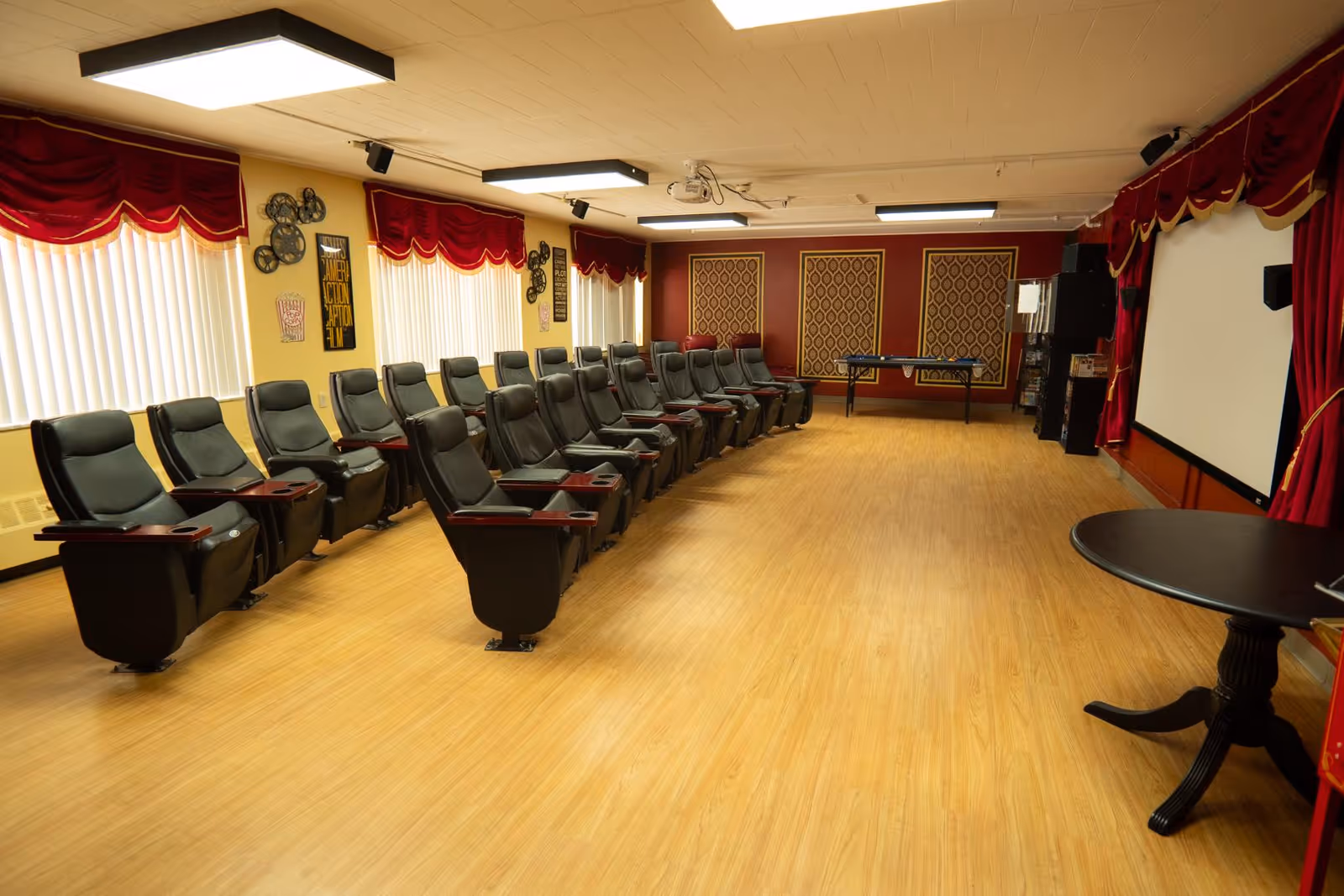 A large interior media room with rows of reclining theater seats facing a projection screen and stage-style curtains.