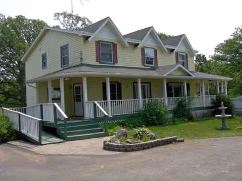 Two-story yellow building with a wraparound porch and landscaped front yard.