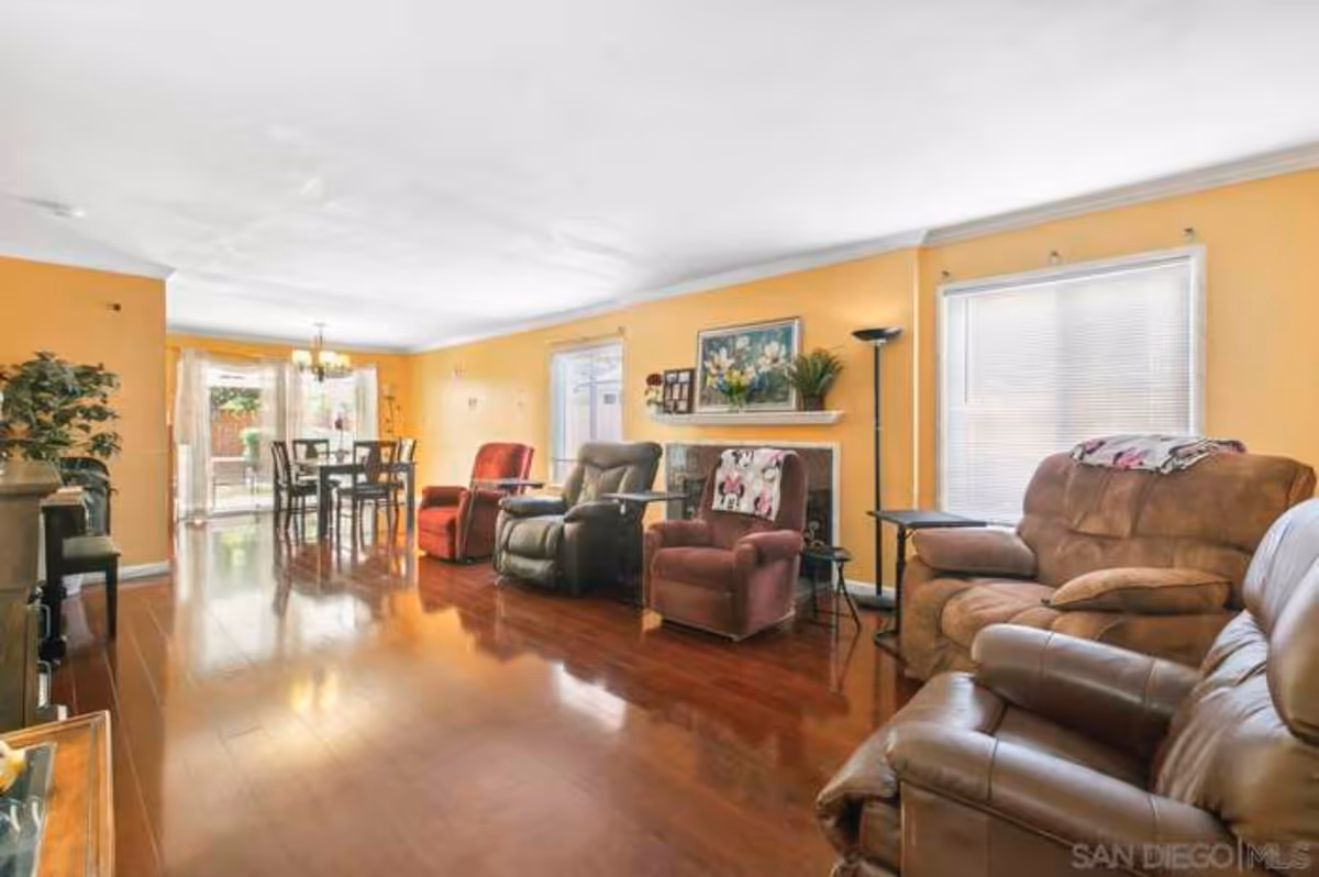 Open living room with several recliner chairs, hardwood floors, yellow walls, a fireplace, and a dining table by sliding glass doors.