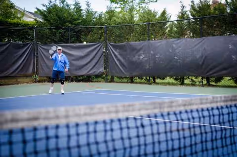 Person in blue shirt playing tennis on an outdoor court at the facility