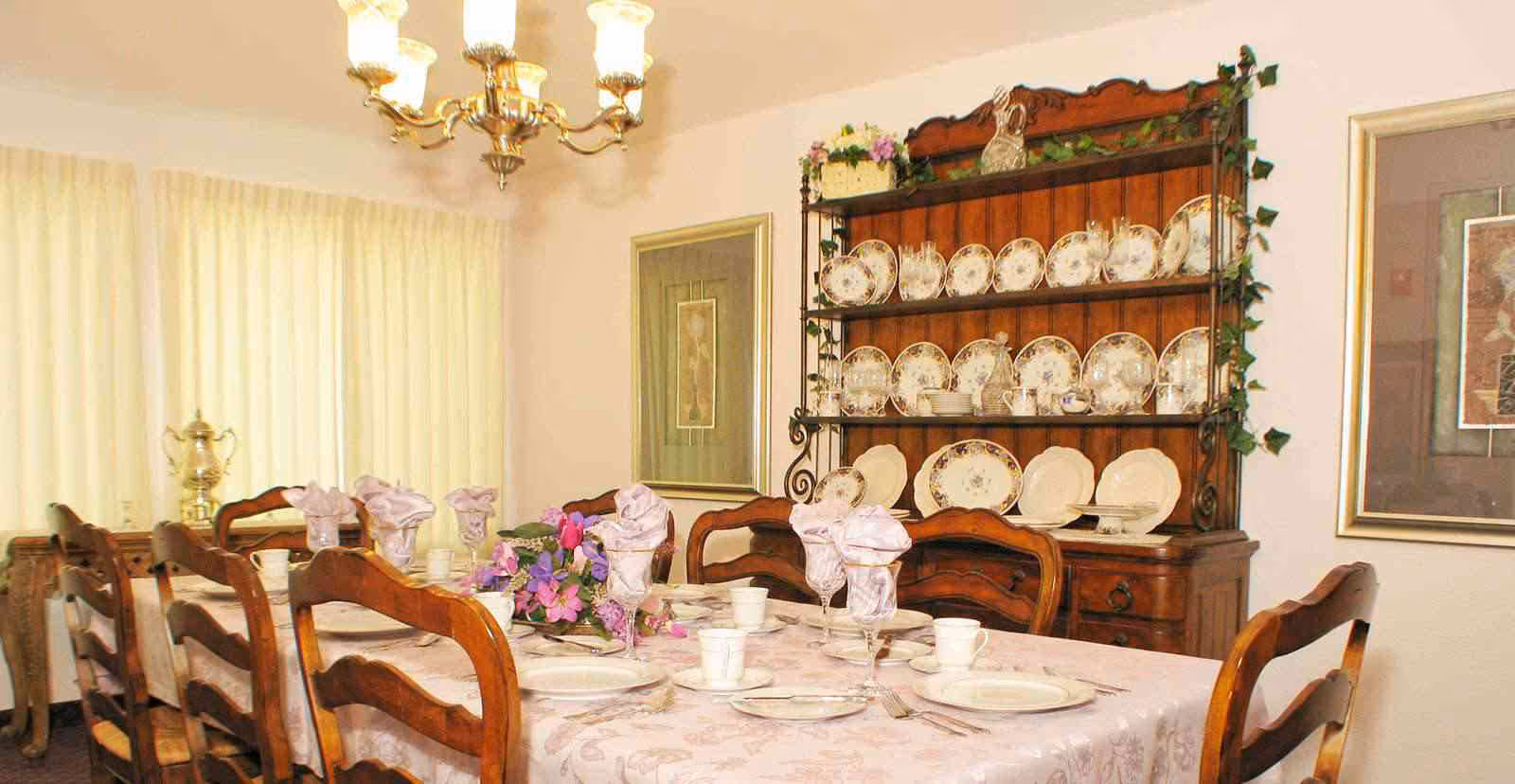 Formal dining room with a set table, wooden chairs, and a china hutch displaying plates.