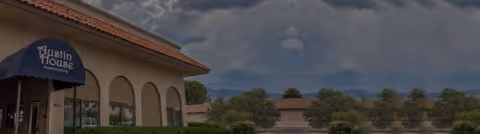 Exterior view of Austin House Assisted Living with arched entrance and blue awning.