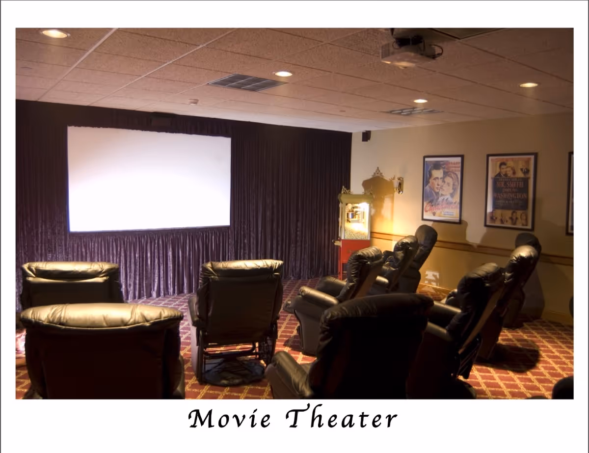A small movie theater room with several black leather recliner chairs arranged in rows facing a large white projection screen. The room has patterned carpet, framed movie posters on the wall, and a popcorn machine in the corner.