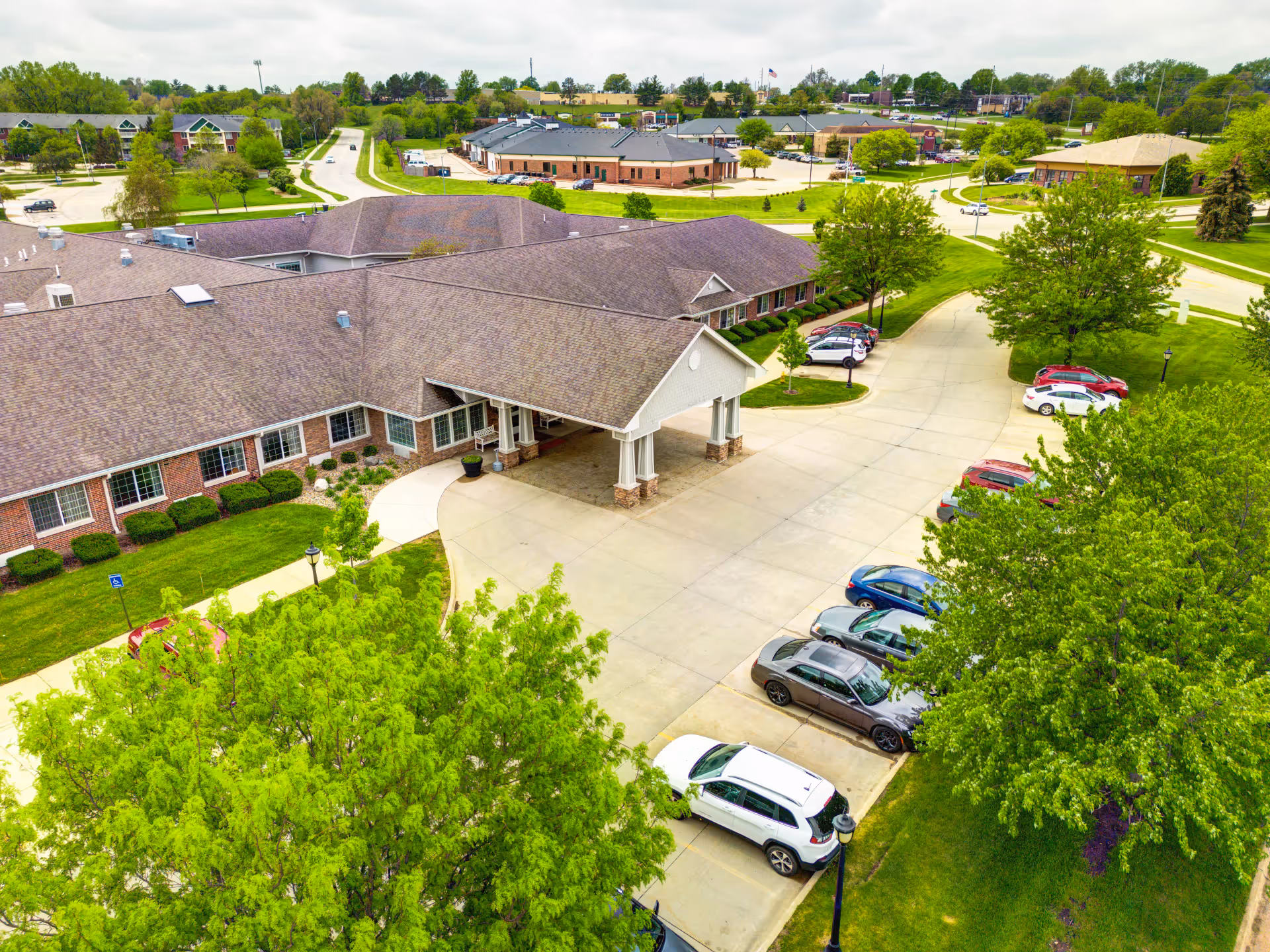 Aerial view of StoryPoint Urbandale's brick building showing a covered entry driveway, parked cars, and surrounding lawns and trees.