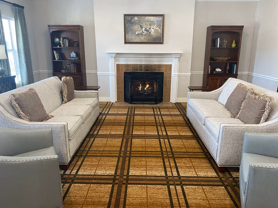 Symmetrical lounge with two sofas facing a central fireplace, flanked by bookshelves and a patterned carpet.