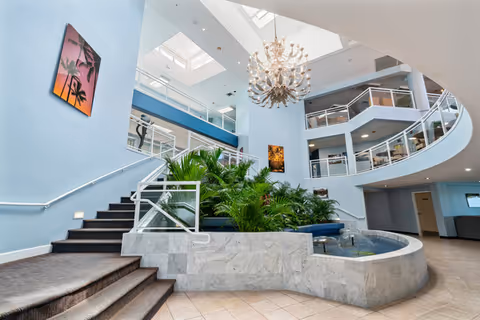 Bright multi-level atrium with a central planter and small fountain, curved balconies, staircase, and a large chandelier.