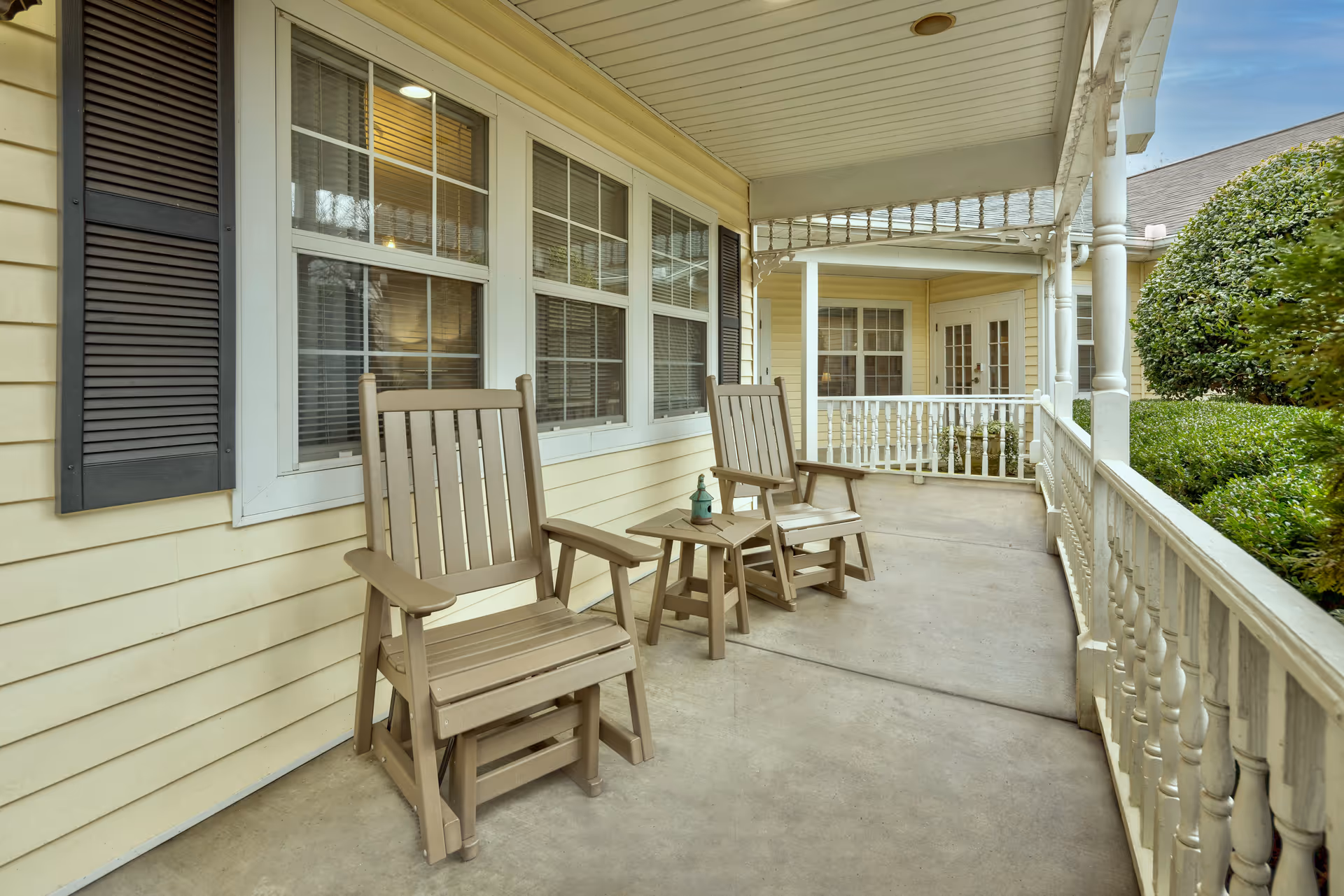Covered front porch with two wooden rocking chairs and a small table along a yellow-sided building.