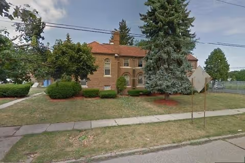 Brick senior living facility with a lawn, trees, and a sidewalk.