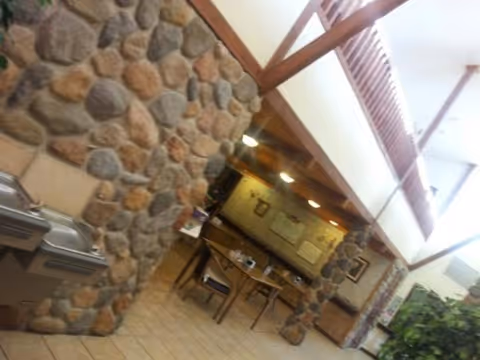 Interior view of a common area with stone pillars and walls, wooden beams on the ceiling, a table with chairs, and water fountains on the left side.